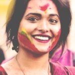 Vibrant portrait of a smiling woman with colorful face paint at Holi festival.